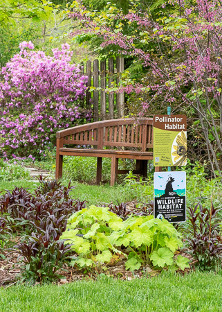 Front yard garden bed featuring informative signs for pollinator and wildlife habitat