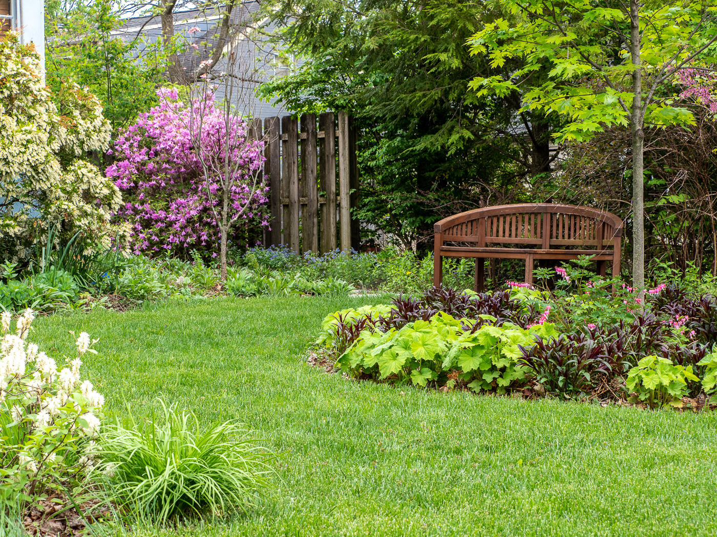 Curving lawn element through colorful garden beds leads to bench area and side yard entry